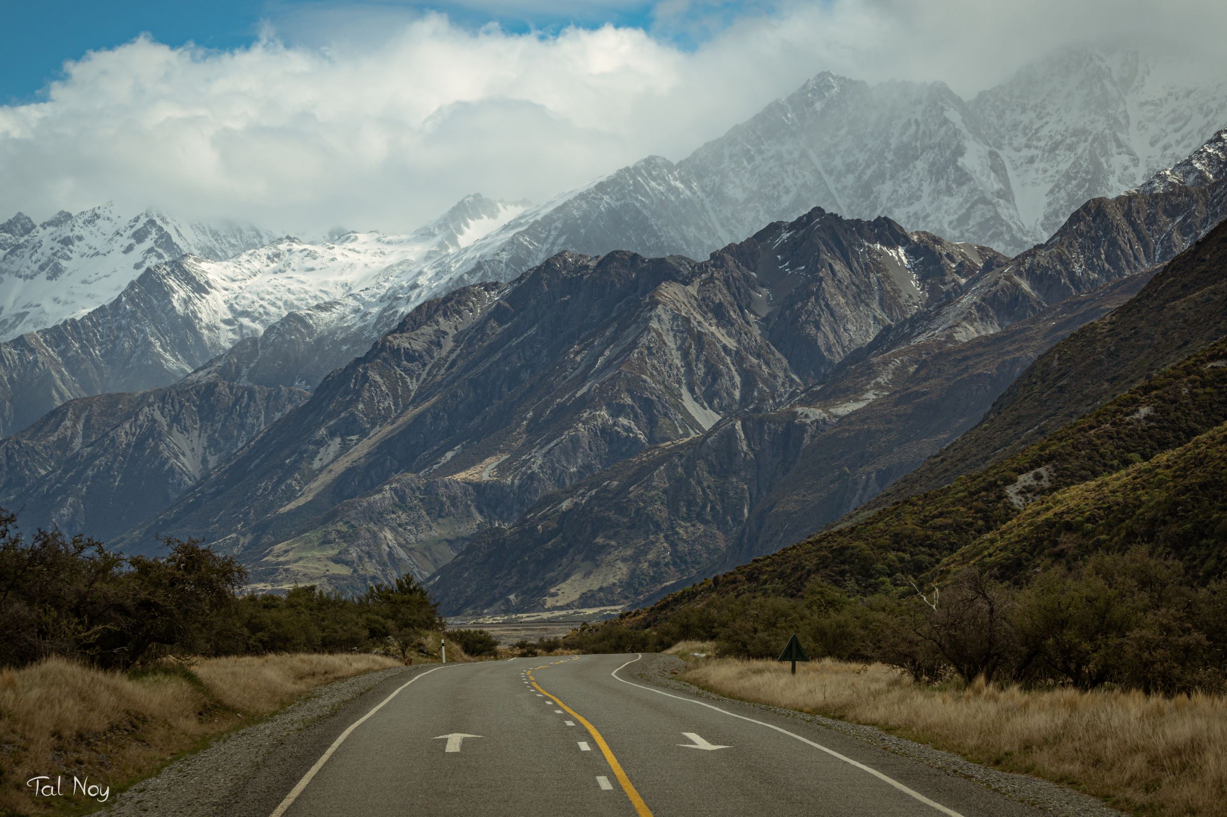 A road curving toward towering snow-capped mountains under dramatic clouds in New Zealand